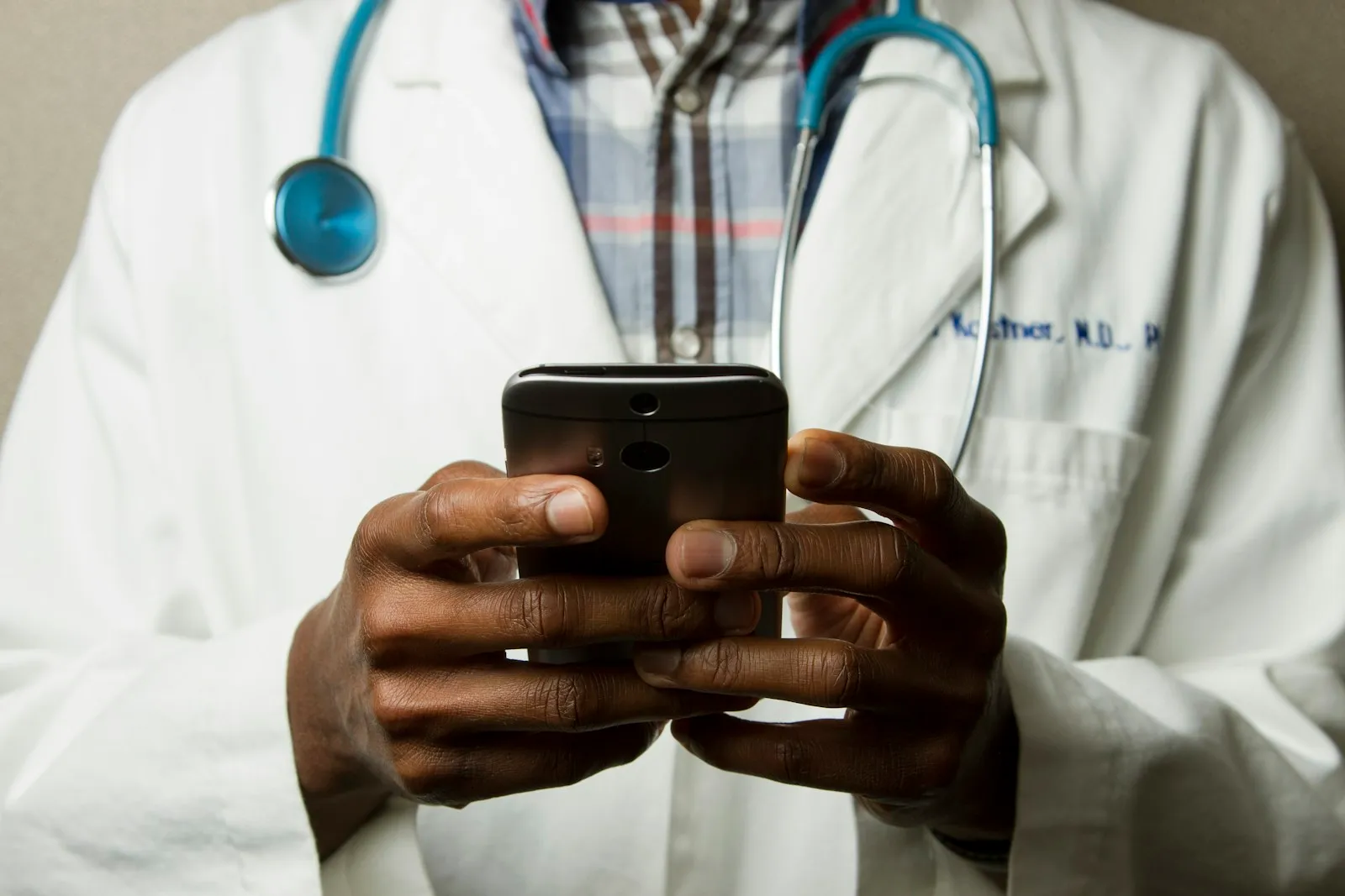 Close-up of a clinician holding a phone, with a stethoscope around their neck