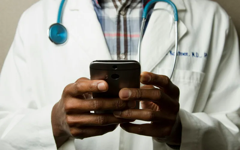 Close-up of a clinician holding a phone, with a stethoscope around their neck