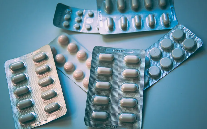 Several blister packs of tablets and capsules on a blue surface