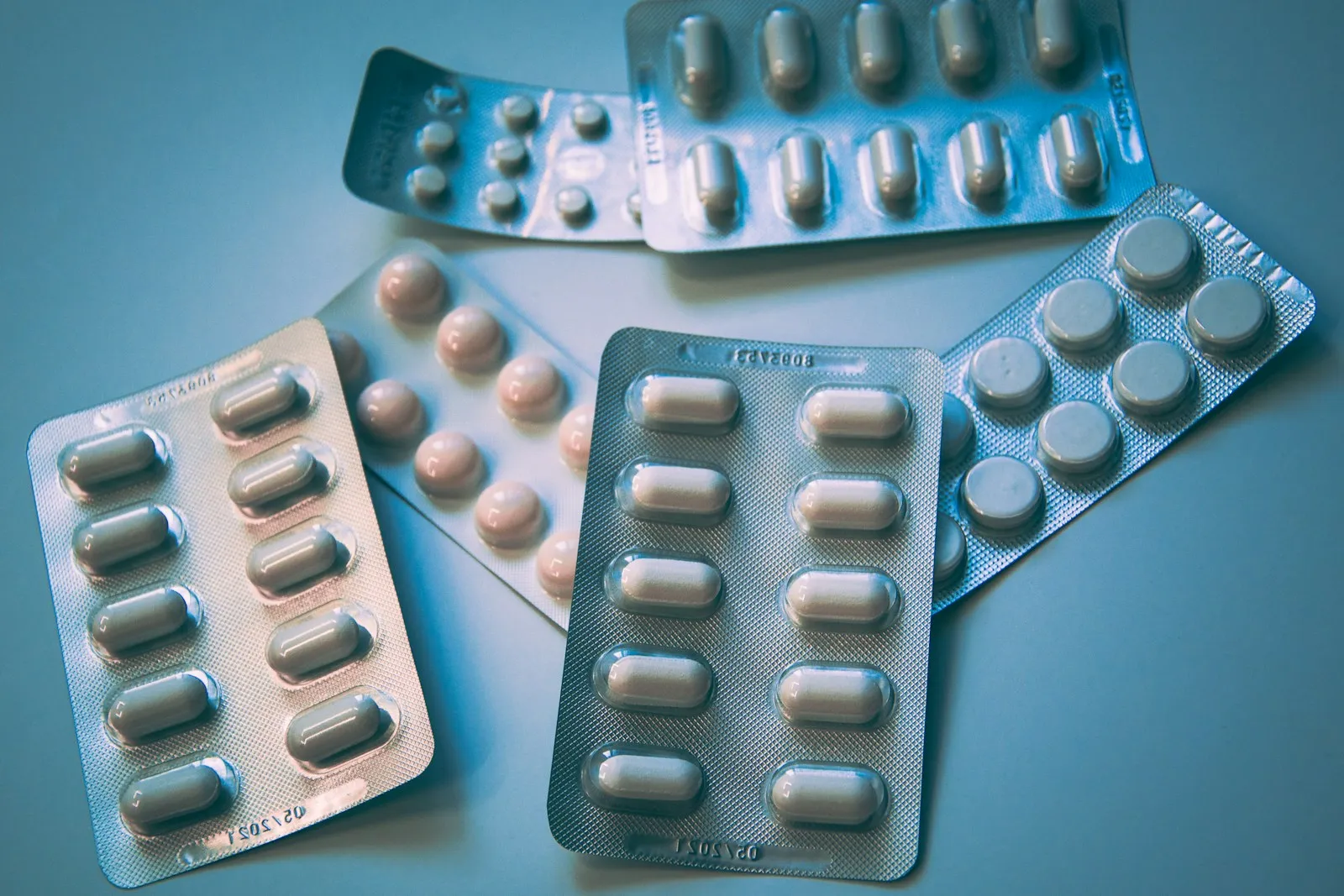 Several blister packs of tablets and capsules on a blue surface
