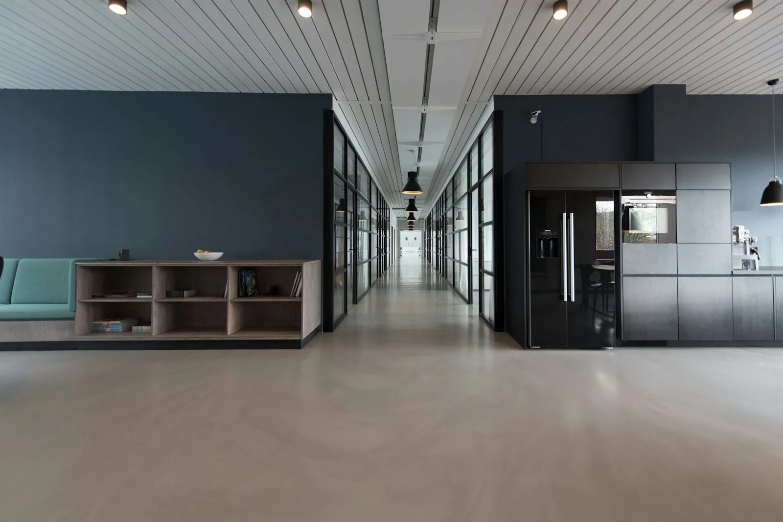 A shared indoor space with seating, a kitchenette, and a glass-lined hallway