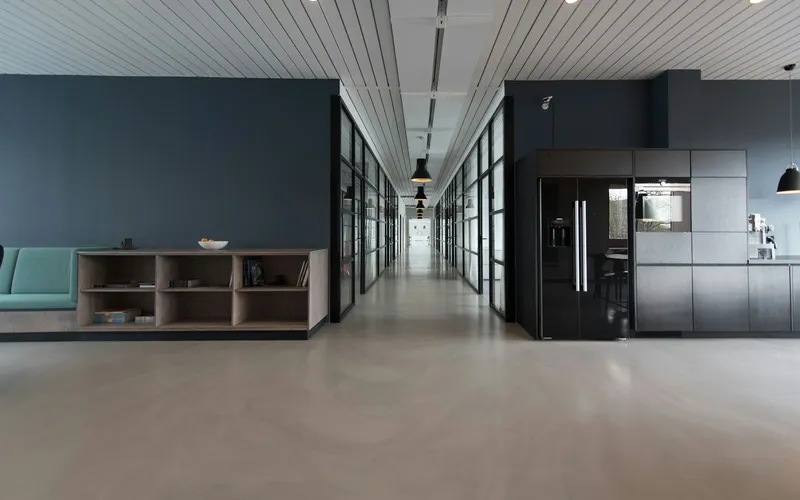 A shared indoor space with seating, a kitchenette, and a glass-lined hallway