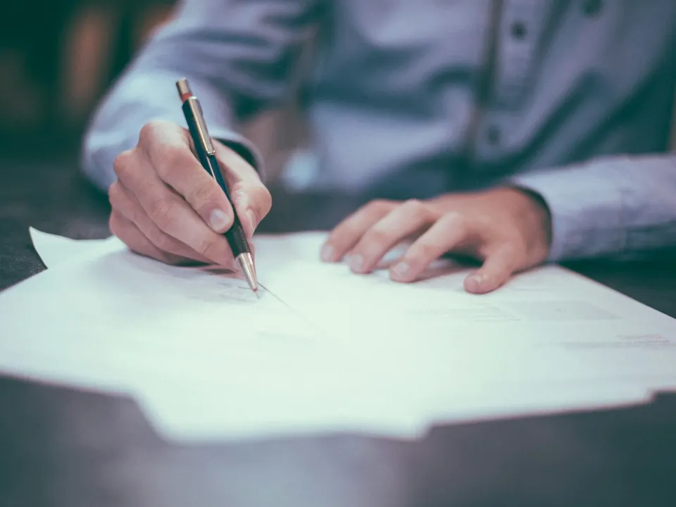 A person at a desk completing paperwork on a laptop