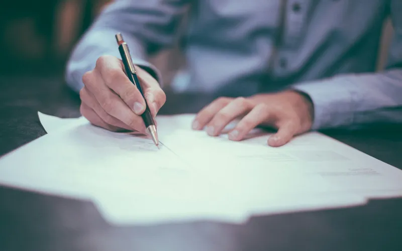 A person writing on a paper document with a pen